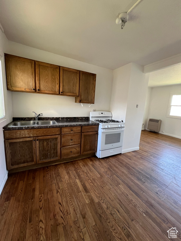 Kitchen with white gas stove, a sink, dark countertops, and dark wood-type flooring