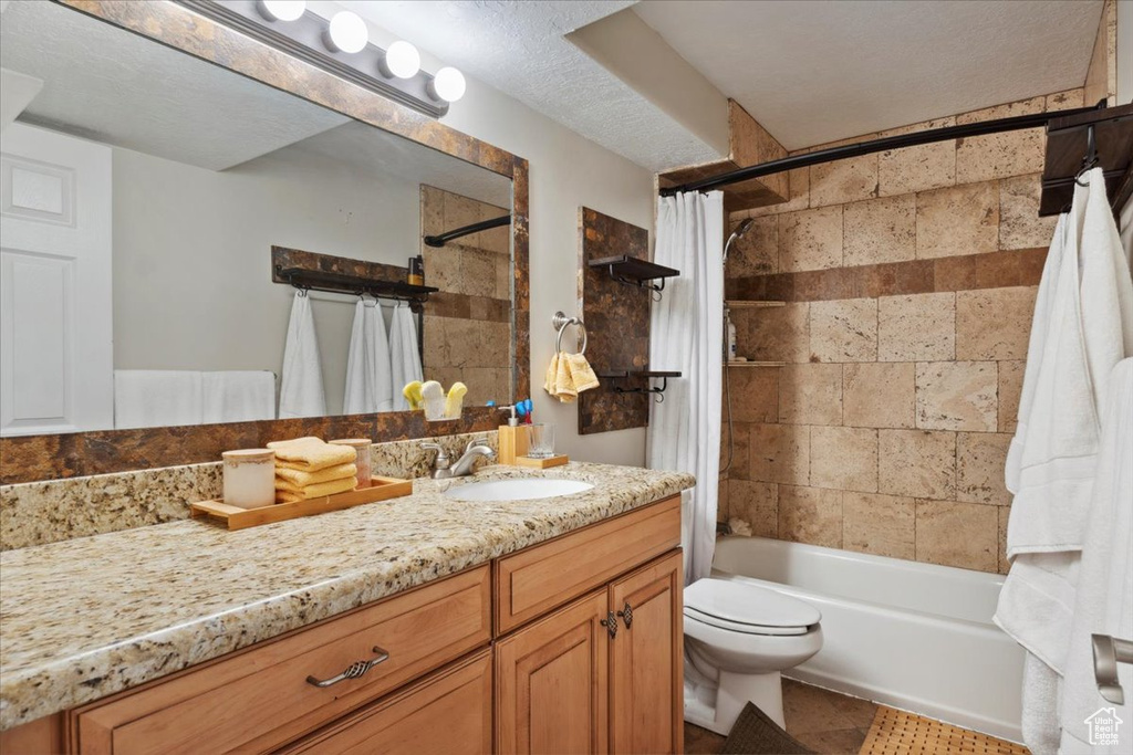 Bathroom featuring vanity, shower / tub combo with curtain, toilet, tile patterned floors, and a textured ceiling