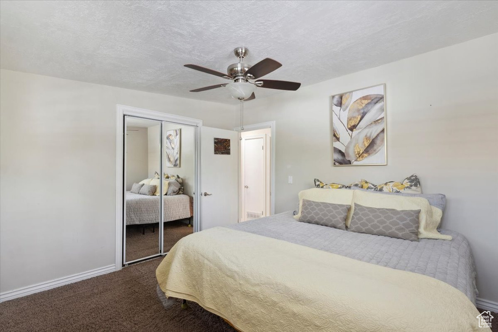 Bedroom with dark colored carpet, baseboards, a closet, a ceiling fan, and a textured ceiling