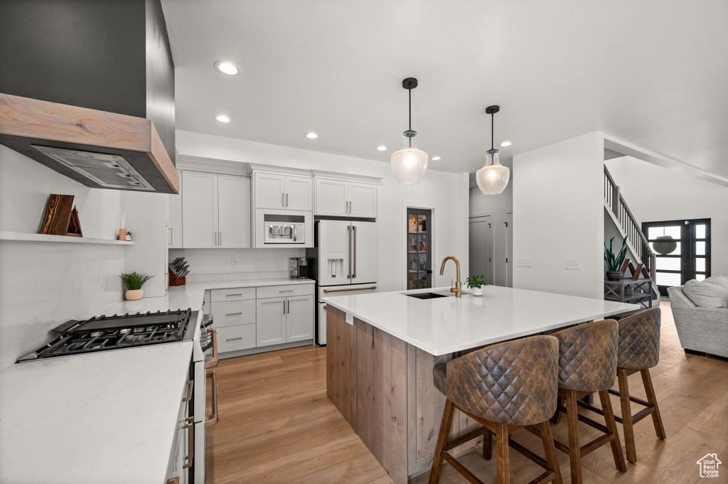 Kitchen featuring wall chimney range hood, a sink, white appliances, light wood-style flooring, and recessed lighting