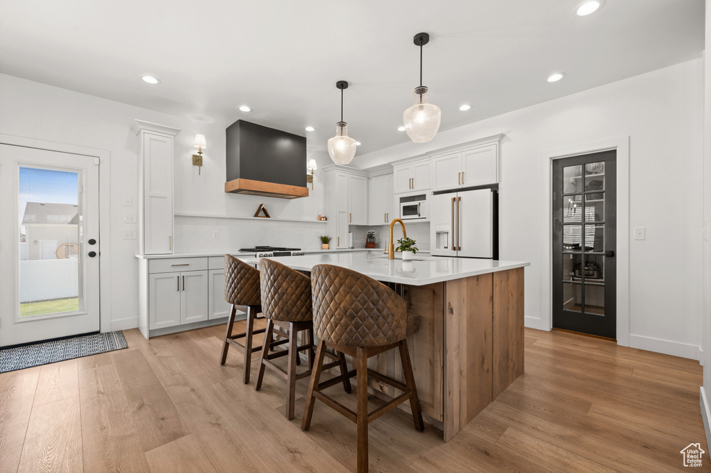 Kitchen featuring high end refrigerator, custom exhaust hood, light countertops, a sink, and recessed lighting
