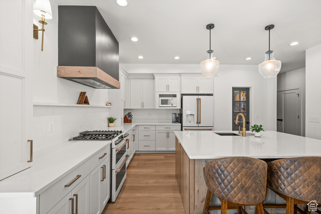 Kitchen with premium appliances, wall chimney range hood, open shelves, a sink, and light countertops