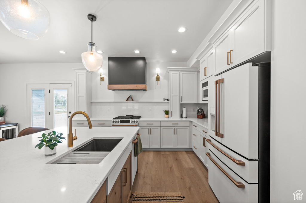 Kitchen featuring white appliances, wall chimney range hood, a sink, recessed lighting, and white cabinetry
