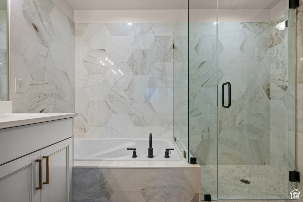 Full bath featuring a garden tub, vanity, and a marble finish shower