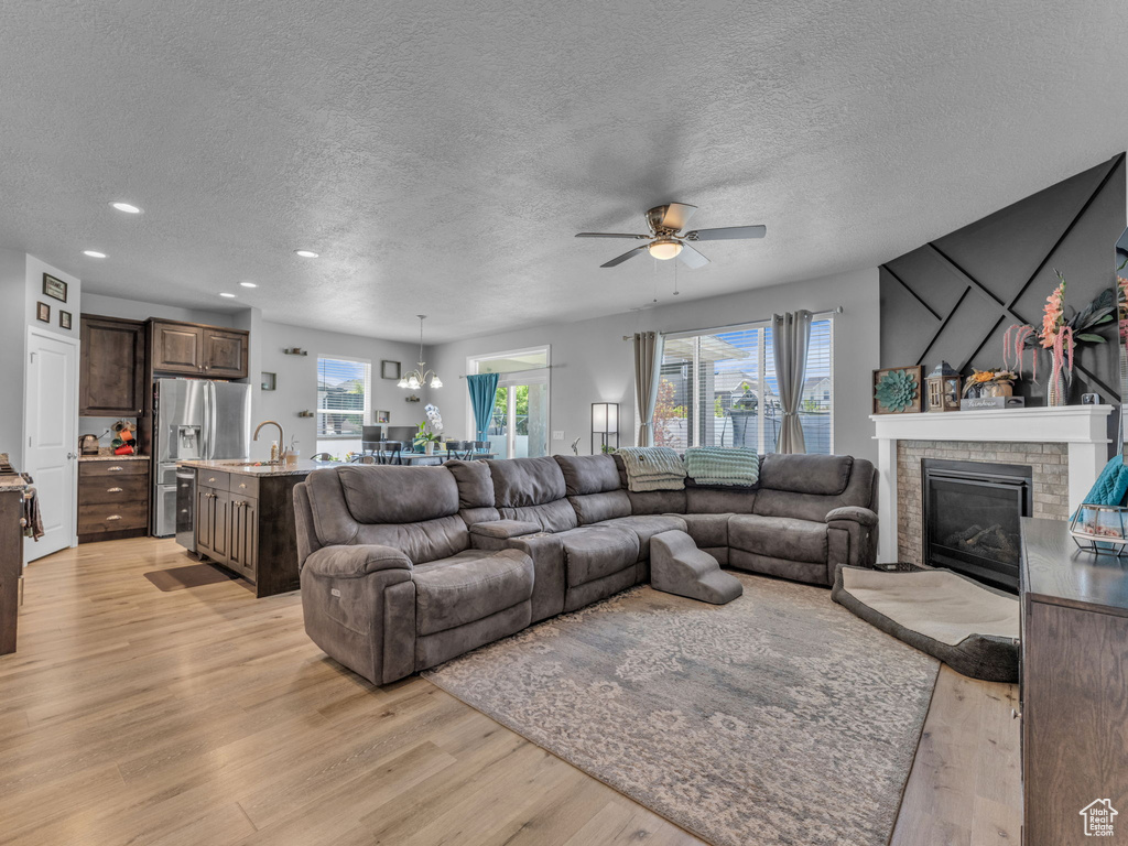 Living room with light wood-style floors, a textured ceiling, a glass covered fireplace, healthy amount of natural light, and ceiling fan