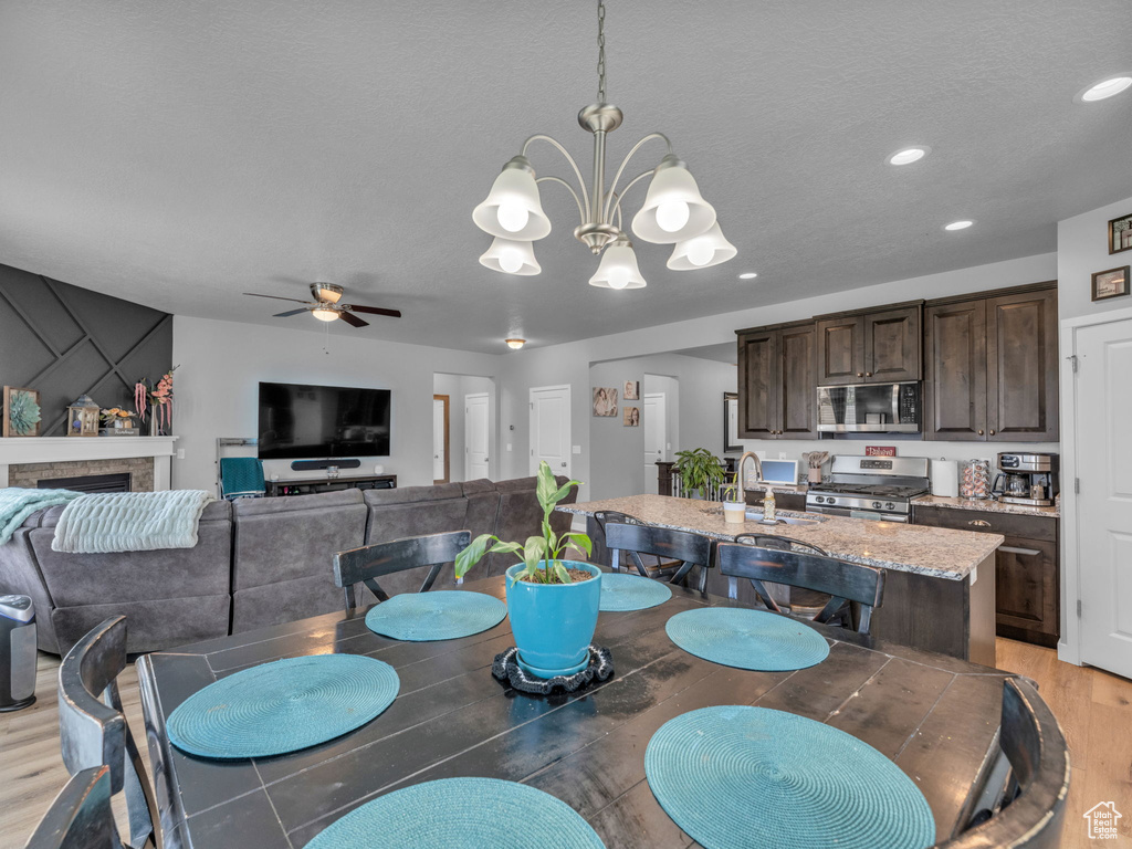 Dining space with light wood finished floors, a ceiling fan, a chandelier, recessed lighting, and a stone fireplace