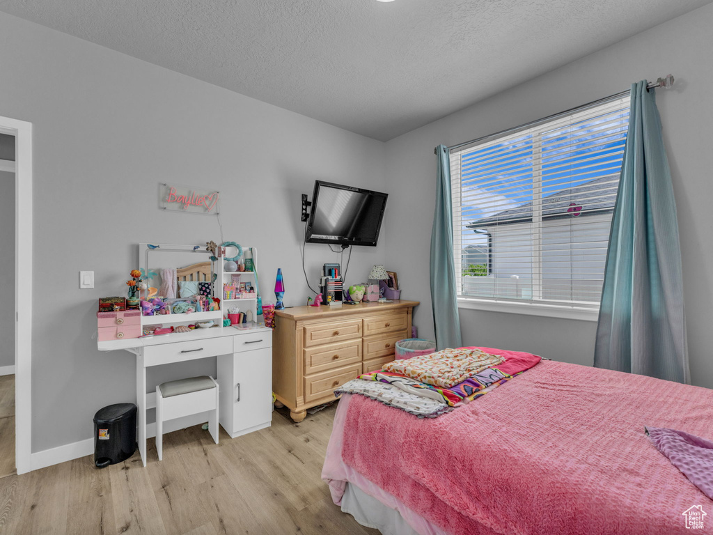 Bedroom with light wood finished floors, baseboards, and a textured ceiling