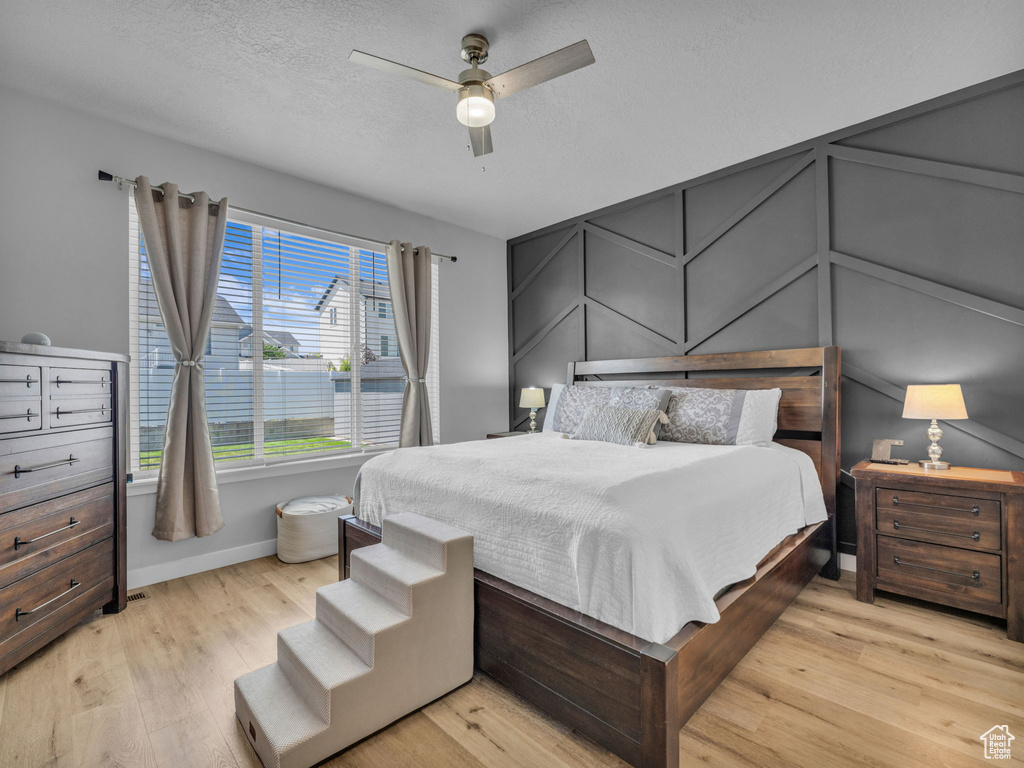 Bedroom with light wood-type flooring, baseboards, a ceiling fan, and a textured ceiling