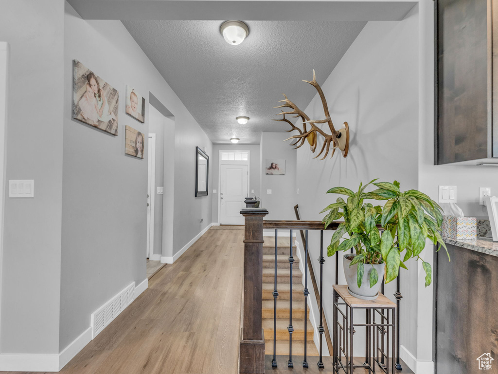Corridor featuring a textured ceiling, baseboards, light wood-type flooring, and an upstairs landing