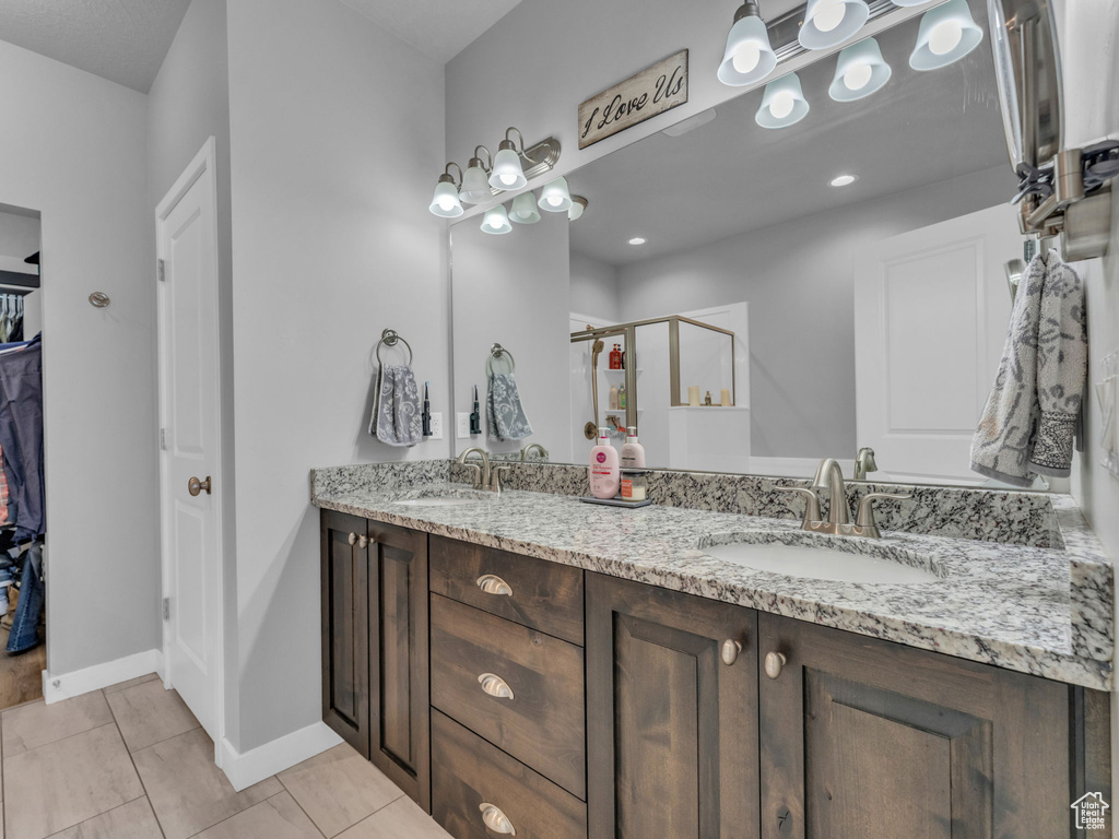 Full bath with double vanity, a stall shower, baseboards, a spacious closet, and tile patterned flooring