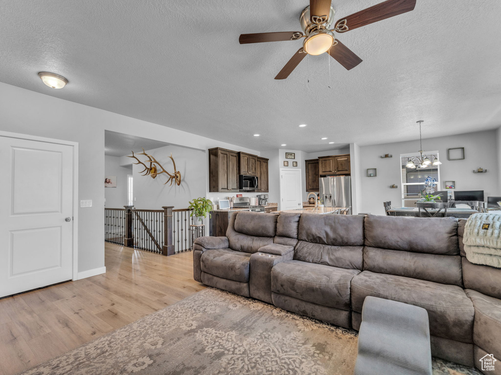 Living room with a textured ceiling, a chandelier, light wood-style flooring, a ceiling fan, and recessed lighting