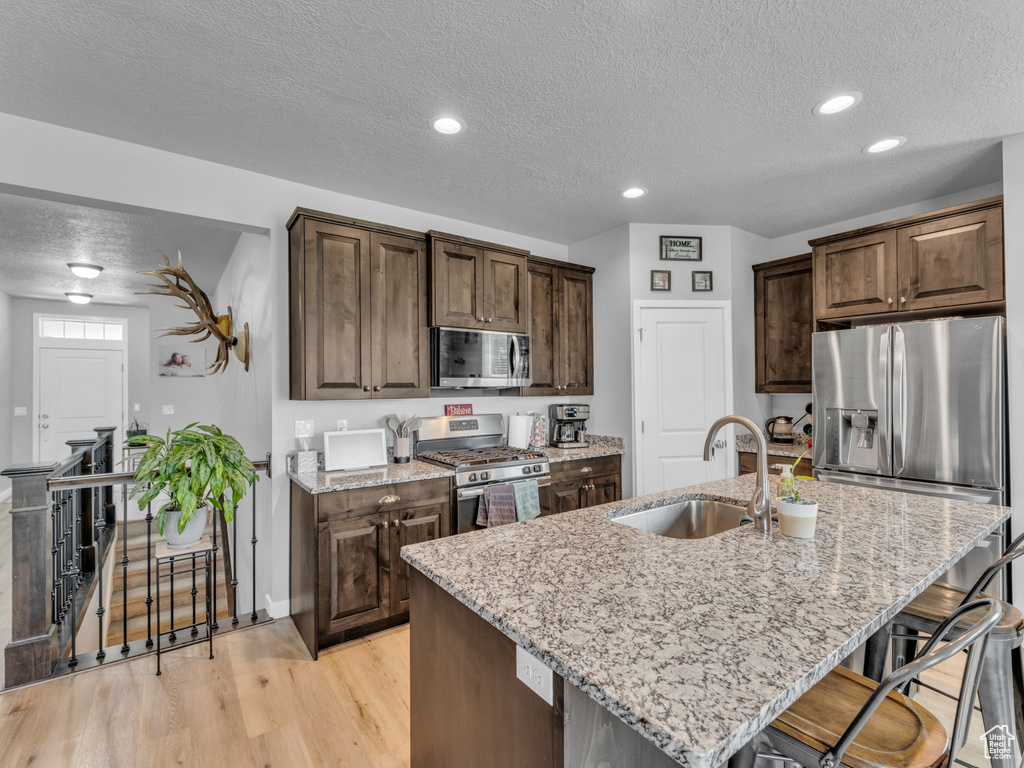 Kitchen featuring stainless steel appliances, a sink, a textured ceiling, light wood-type flooring, and light stone countertops