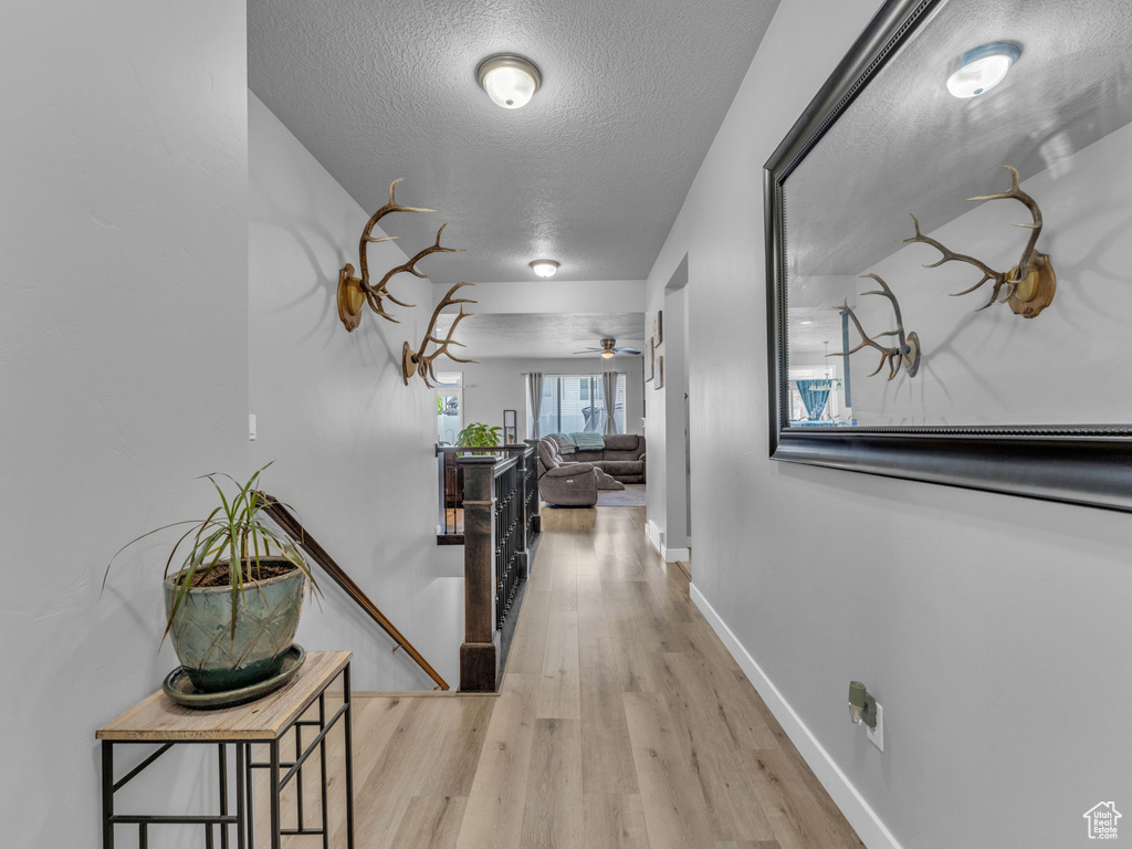 Corridor with a textured ceiling, an upstairs landing, wood finished floors, and baseboards