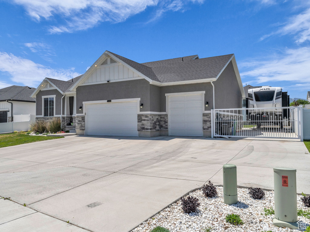 View of front facade featuring a garage, driveway, stone siding, and stucco siding