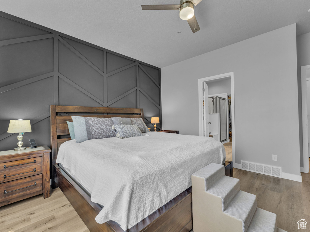 Bedroom with a decorative wall, light wood-type flooring, baseboards, ceiling fan, and a spacious closet