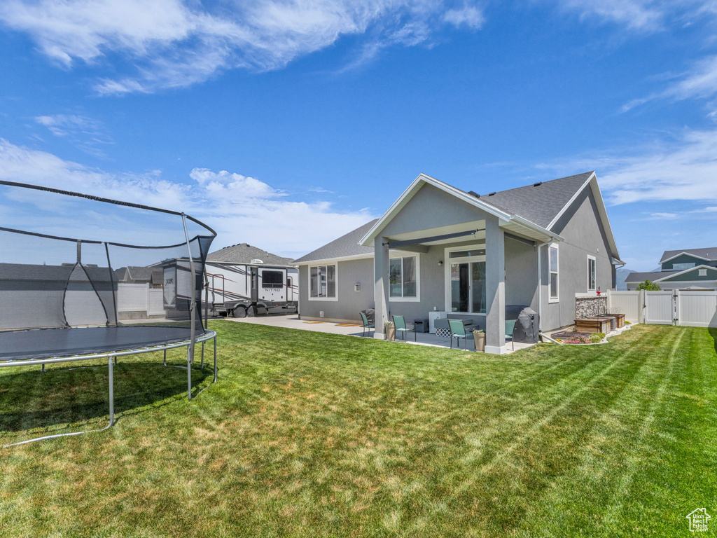 Back of property featuring a trampoline, a patio, stucco siding, outdoor lounge area, and a gate