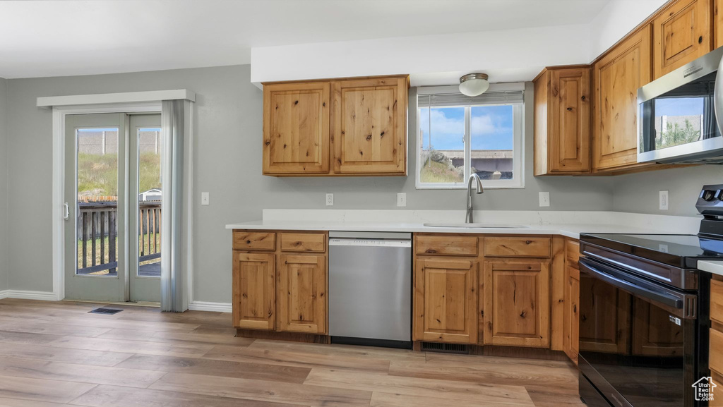 Kitchen with stainless steel appliances, a sink, light wood finished floors, light countertops, and brown cabinets