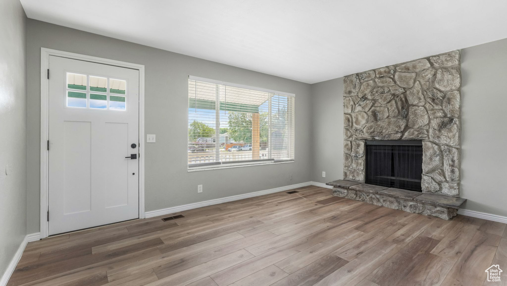 Unfurnished living room with healthy amount of natural light, wood finished floors, a stone fireplace, and baseboards