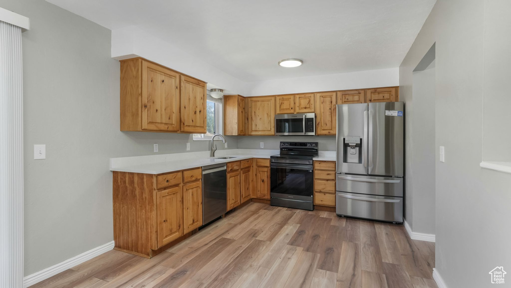 Kitchen with stainless steel appliances, a sink, light wood-style floors, light countertops, and baseboards