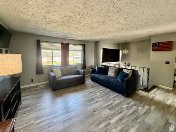 Living room with wood finished floors, a textured ceiling, a chandelier, and baseboards