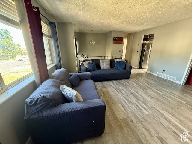 Living room with a textured ceiling, light wood-style flooring, baseboards, and a chandelier
