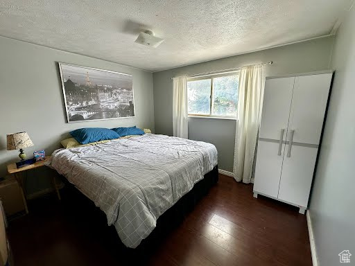 Bedroom with dark wood-style flooring, a textured ceiling, and baseboards