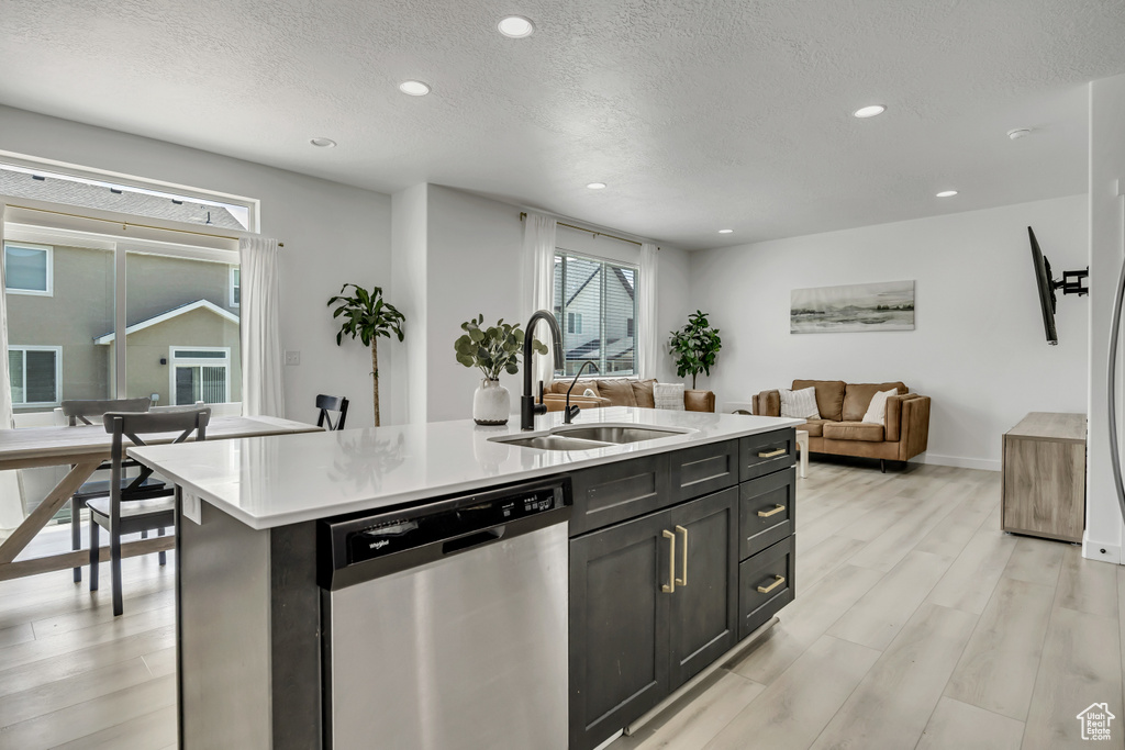 Kitchen with dishwasher, a sink, light countertops, light wood-style flooring, and a textured ceiling