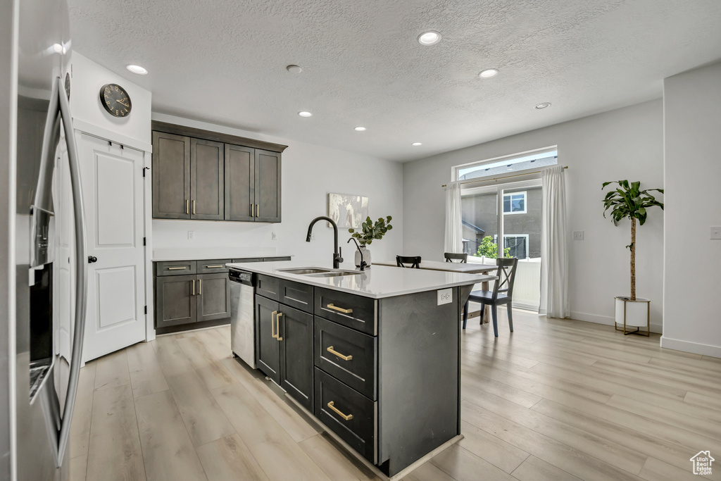 Kitchen featuring a sink, stainless steel appliances, a textured ceiling, light wood-type flooring, and light countertops