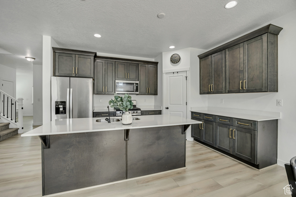 Kitchen with appliances with stainless steel finishes, a kitchen island with sink, light countertops, dark brown cabinets, and recessed lighting