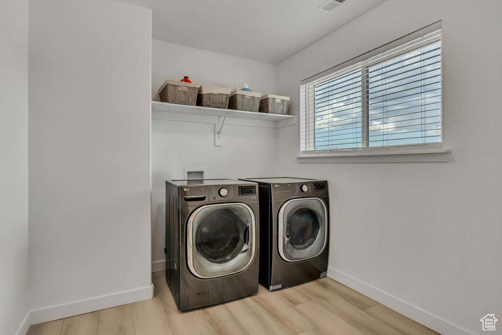 Laundry room with independent washer and dryer, baseboards, and light wood-style floors