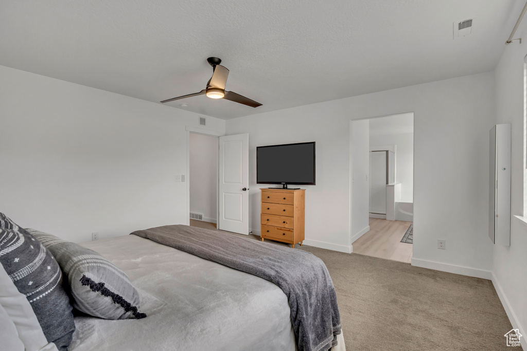 Bedroom with light colored carpet, ceiling fan, baseboards, and ensuite bathroom