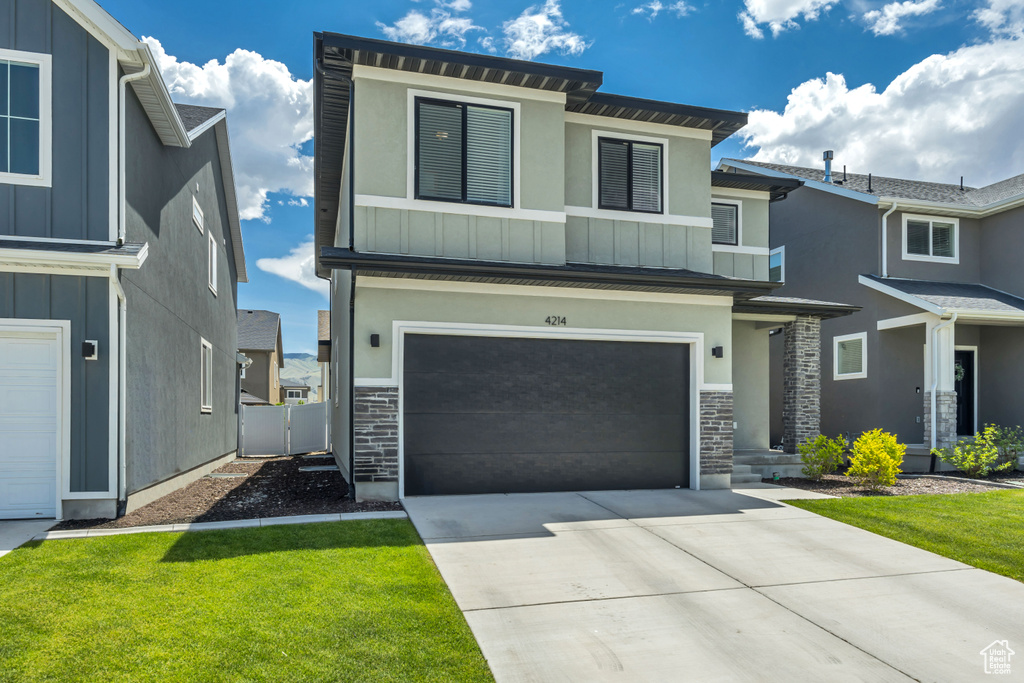 Contemporary home featuring board and batten siding, stone siding, an attached garage, and concrete driveway