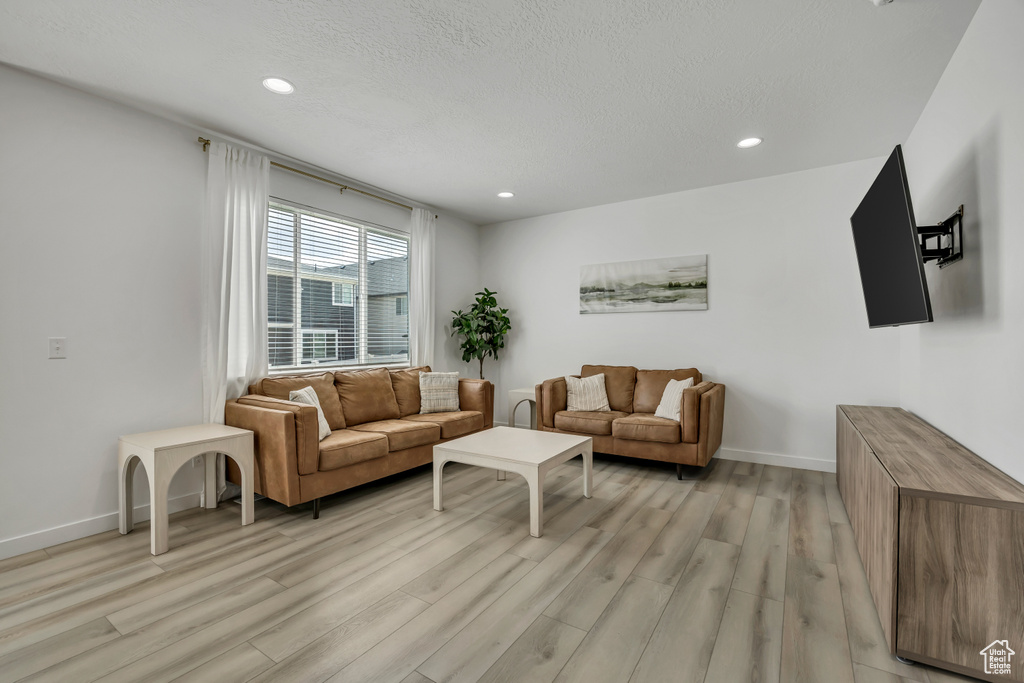 Living area with light wood-type flooring, recessed lighting, baseboards, and a textured ceiling