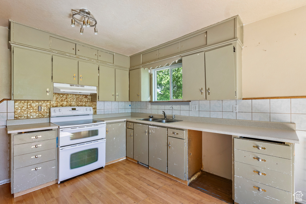Kitchen featuring range with two ovens, under cabinet range hood, a sink, light wood-style floors, and light countertops