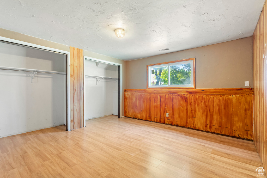 Unfurnished bedroom with two closets, light wood-type flooring, wainscoting, and wooden walls