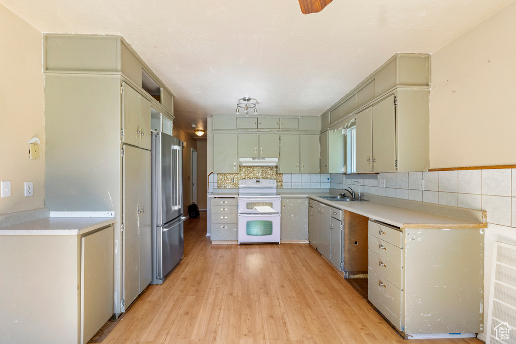 Kitchen with double oven range, freestanding refrigerator, a sink, under cabinet range hood, and light wood finished floors