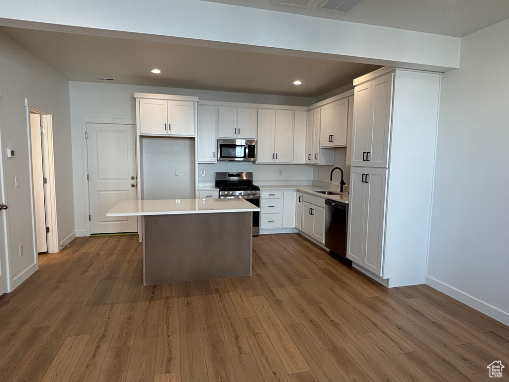 Kitchen with stainless steel appliances, white cabinets, wood finished floors, a center island, and a sink