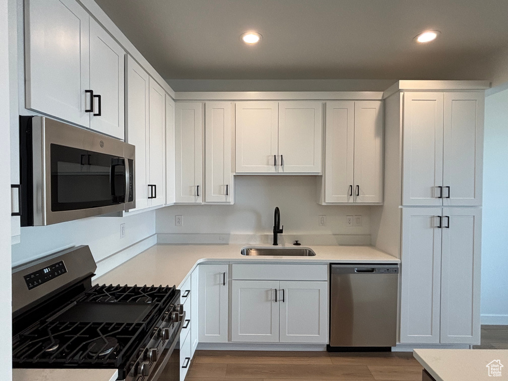 Kitchen with appliances with stainless steel finishes, a sink, recessed lighting, light wood finished floors, and white cabinetry