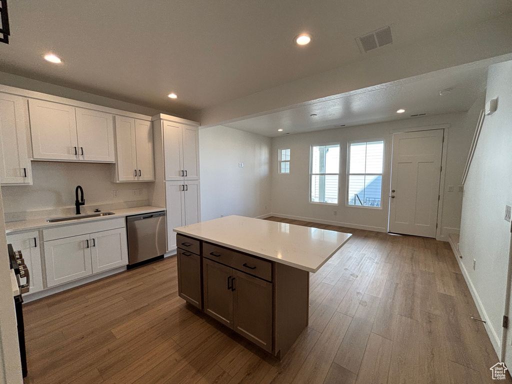 Kitchen with dishwasher, a sink, wood finished floors, light countertops, and recessed lighting