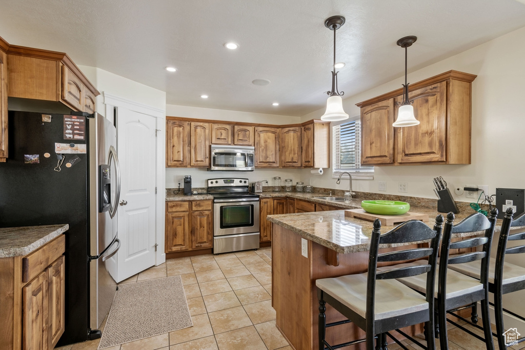 Kitchen with appliances with stainless steel finishes, a peninsula, a sink, brown cabinets, and hanging light fixtures