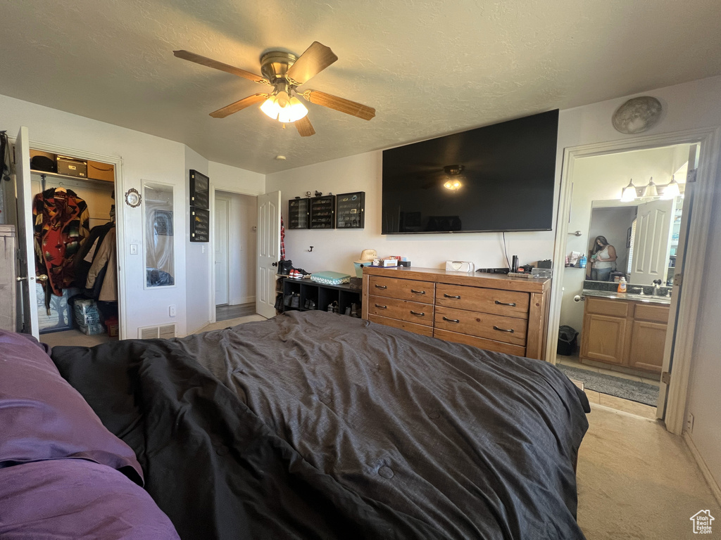 Bedroom featuring light carpet, ensuite bathroom, a ceiling fan, a walk in closet, and a closet
