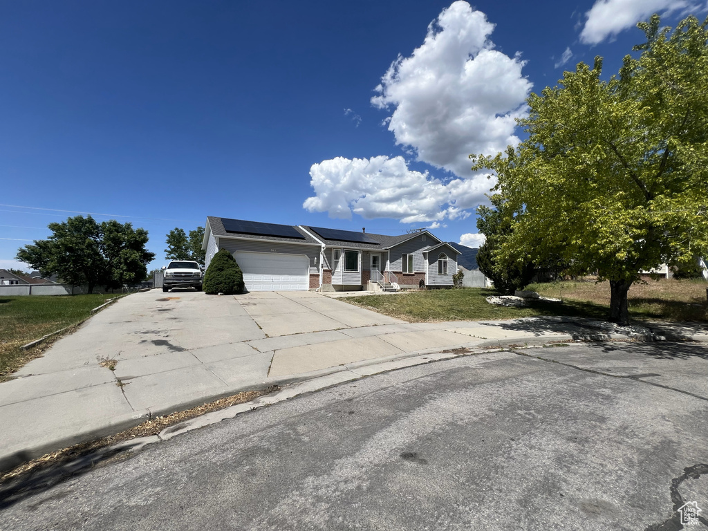 Ranch-style home with driveway, solar panels, an attached garage, brick siding, and a front yard