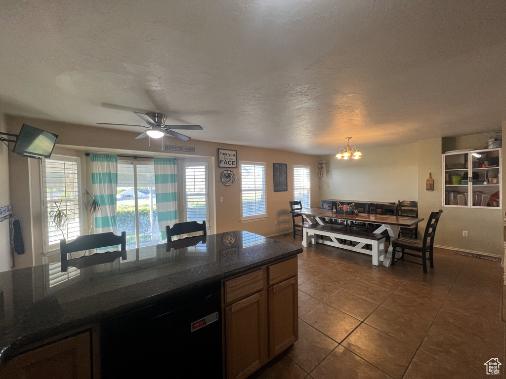 Kitchen with dark tile patterned flooring, a chandelier, a ceiling fan, dishwasher, and dark stone countertops