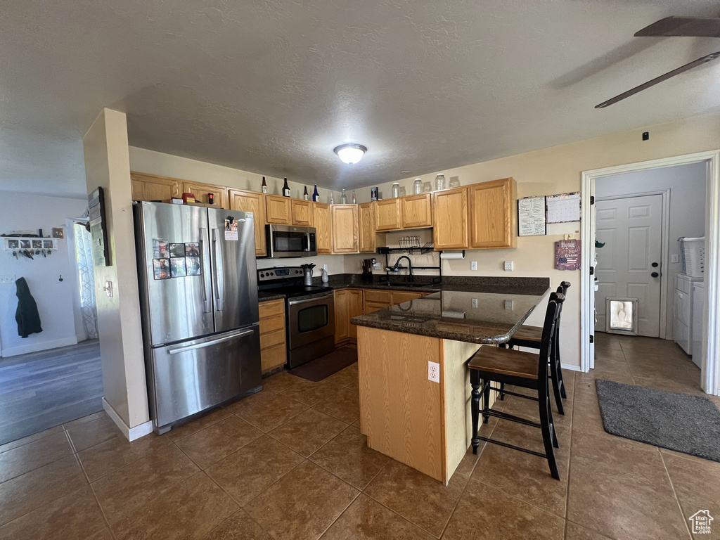 Kitchen featuring appliances with stainless steel finishes, a sink, ceiling fan, dark countertops, and a kitchen bar
