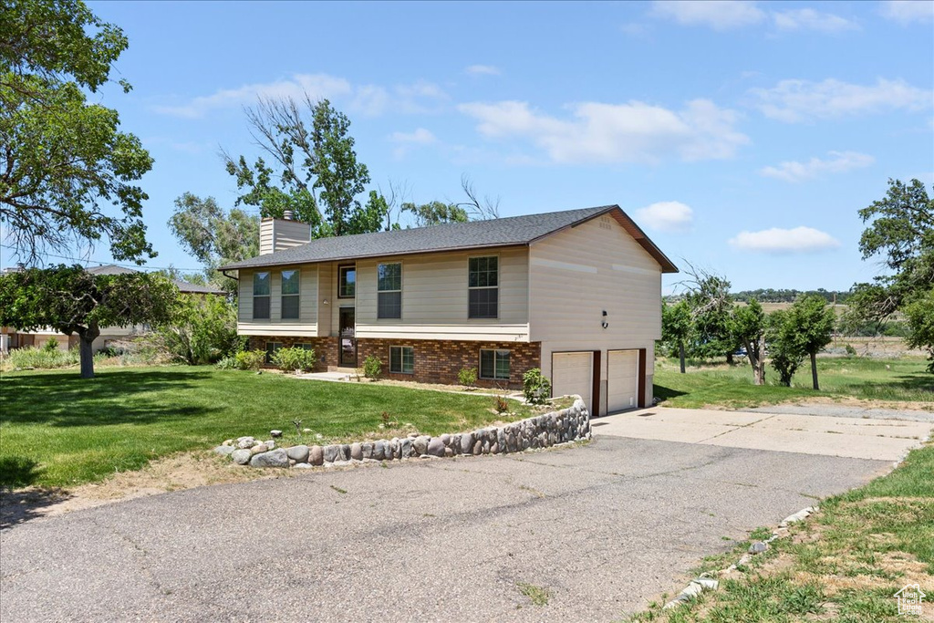 View of front facade featuring a garage, a chimney, a front lawn, driveway, and brick siding