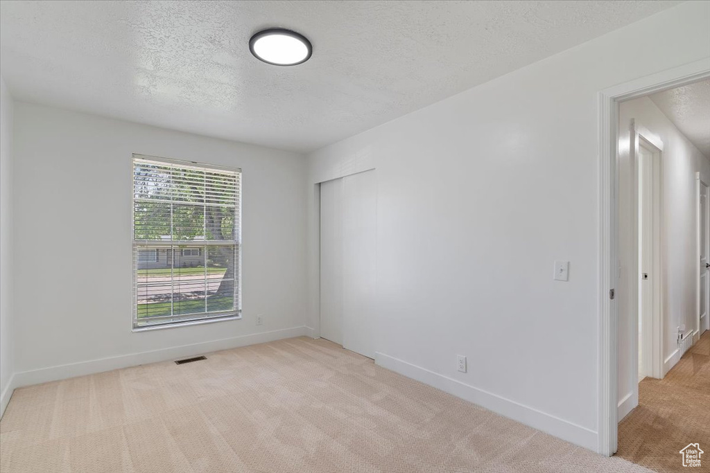 Empty room with light carpet, baseboards, and a textured ceiling