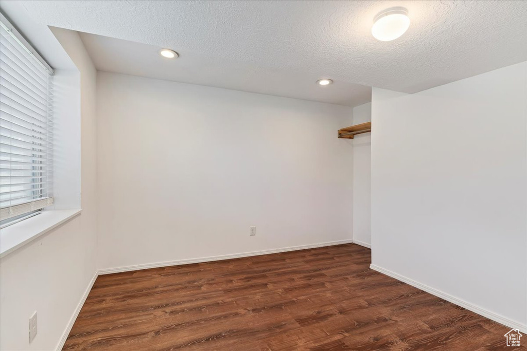 Empty room featuring dark wood-style floors, recessed lighting, baseboards, and a textured ceiling