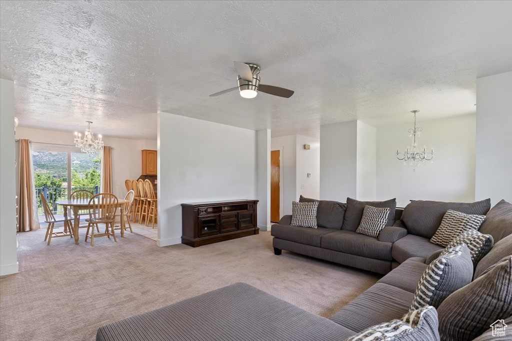 Living area featuring a chandelier, light carpet, a ceiling fan, a textured ceiling, and baseboards