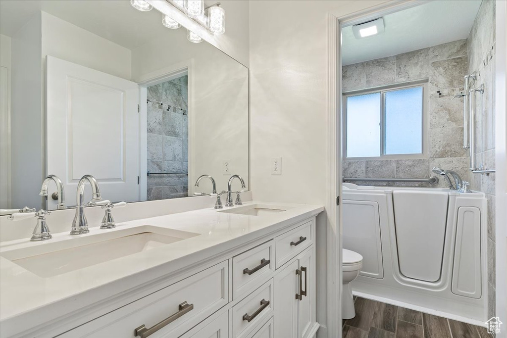 Full bath with a tub to relax in, double vanity, toilet, wood finished floors, and a shower