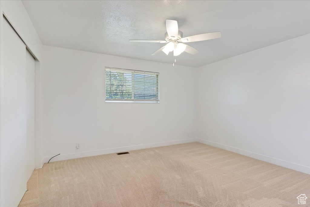 Empty room featuring light carpet, a ceiling fan, and baseboards